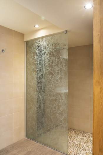 Cabine de douche moderne avec paroi en verre texturé et sol en galets.<br />